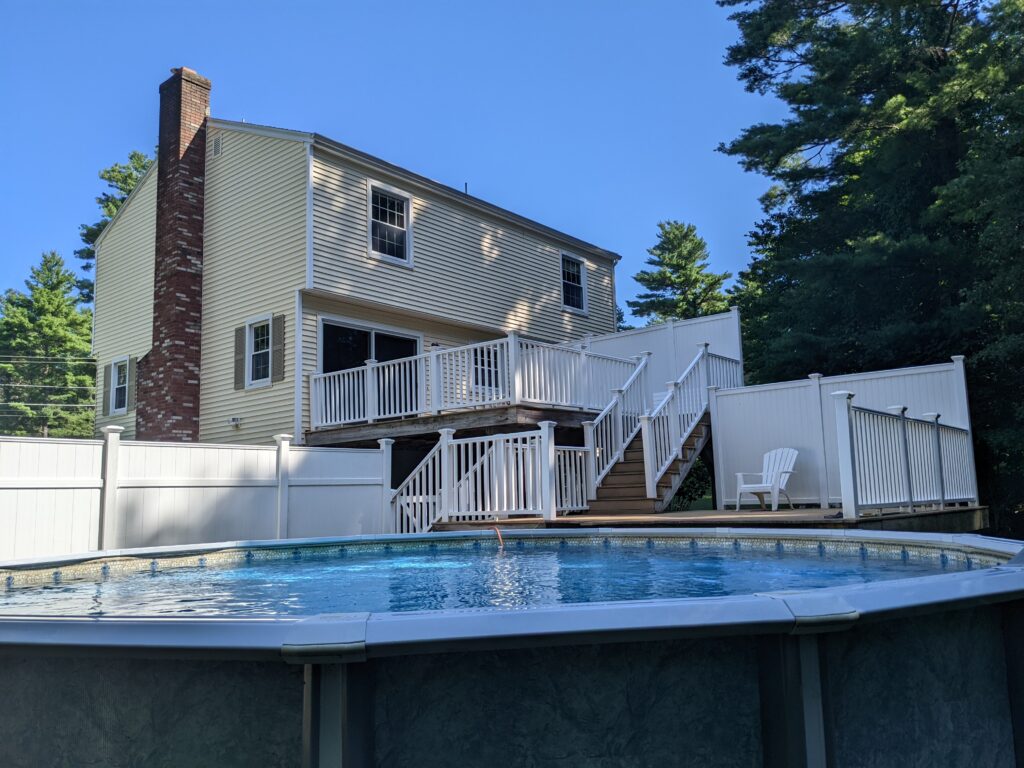split two-story yellow home with back deck leading down to swimming pool