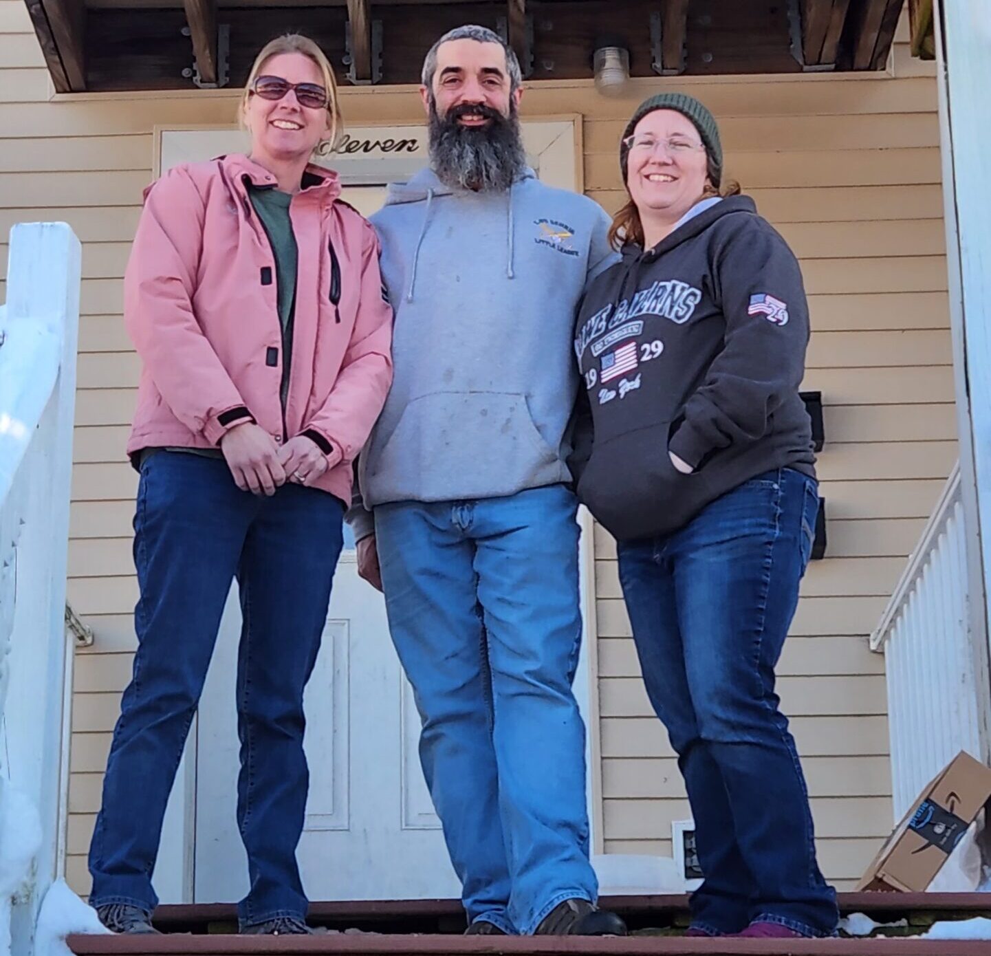 three people smiling in front of house