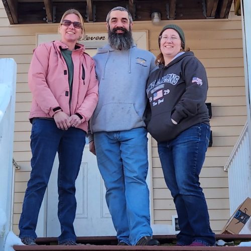 three people smiling in front of house